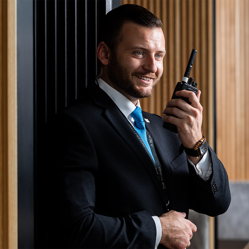 A male security guard smiling and speaking into his radio