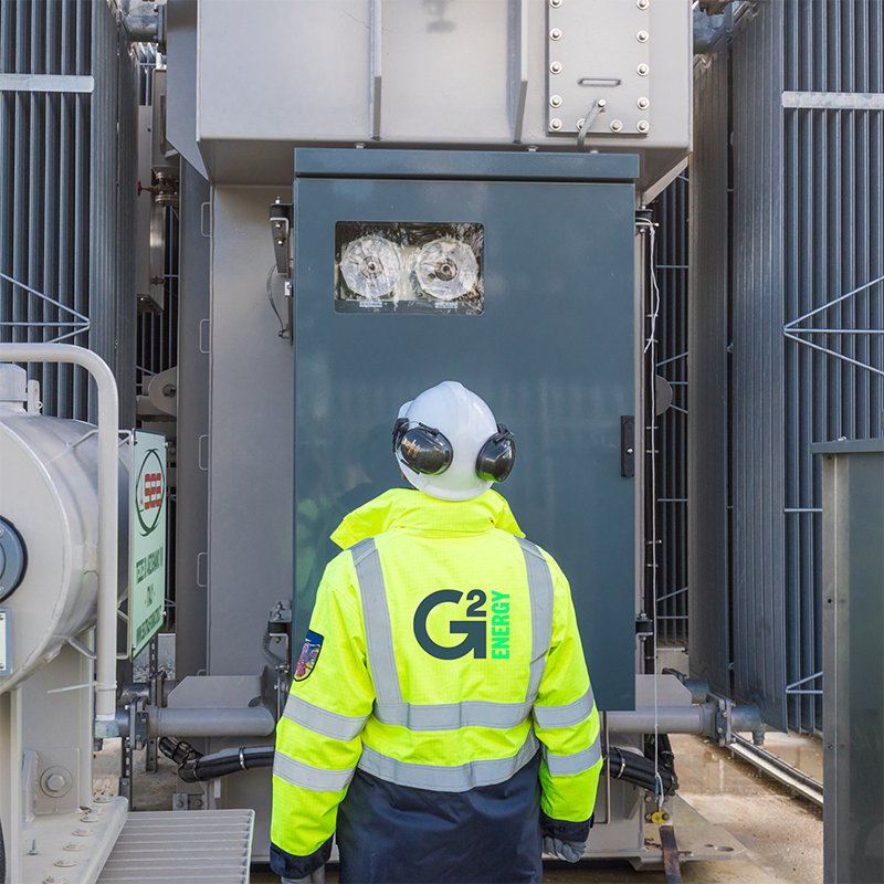 A G2 Energy engineer in a hard hat and high vis jacket, standing in front of industry plant material