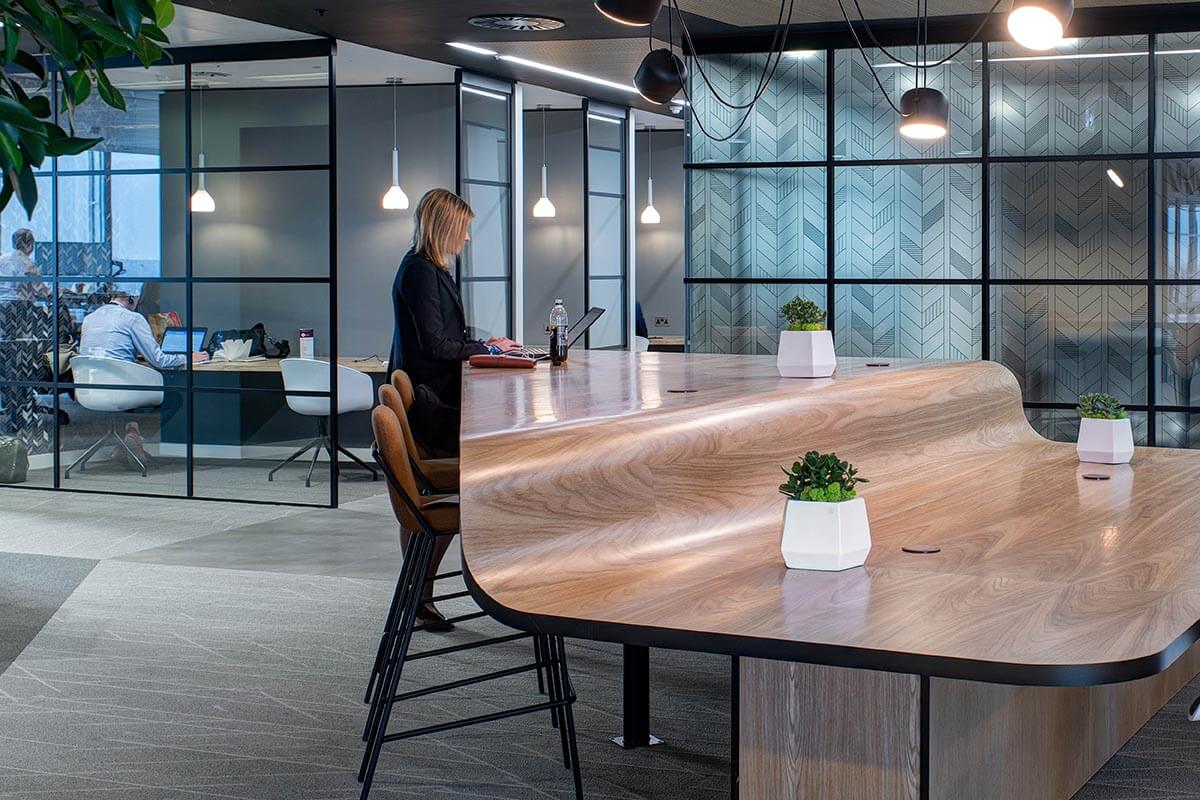 A women using a laptop at a standing desk, in a modern open-plan office space