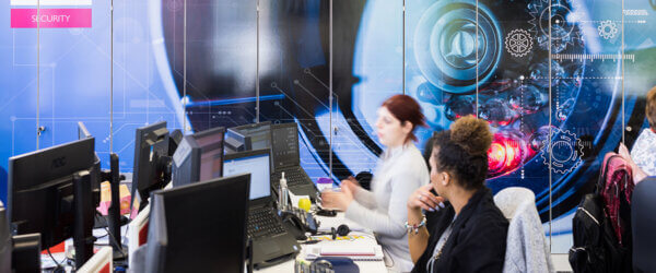 Mitie TSOC security centre - people sitting at rows of desks with computers, with a large screen of data in the UK showing on the far wall