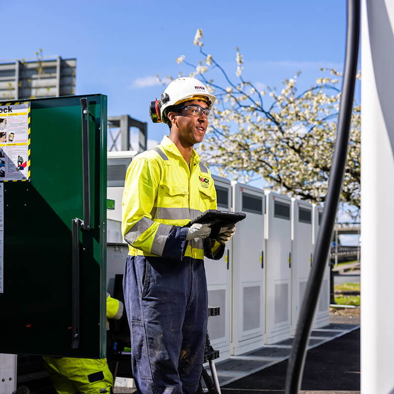 Rock Power Connections engineer dressed in a hard hat and high vis overalls, holding an iPad