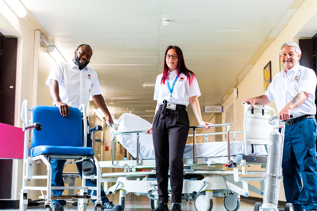 Three Mitie workers standing in a hospital corridor with various healthcare equipment