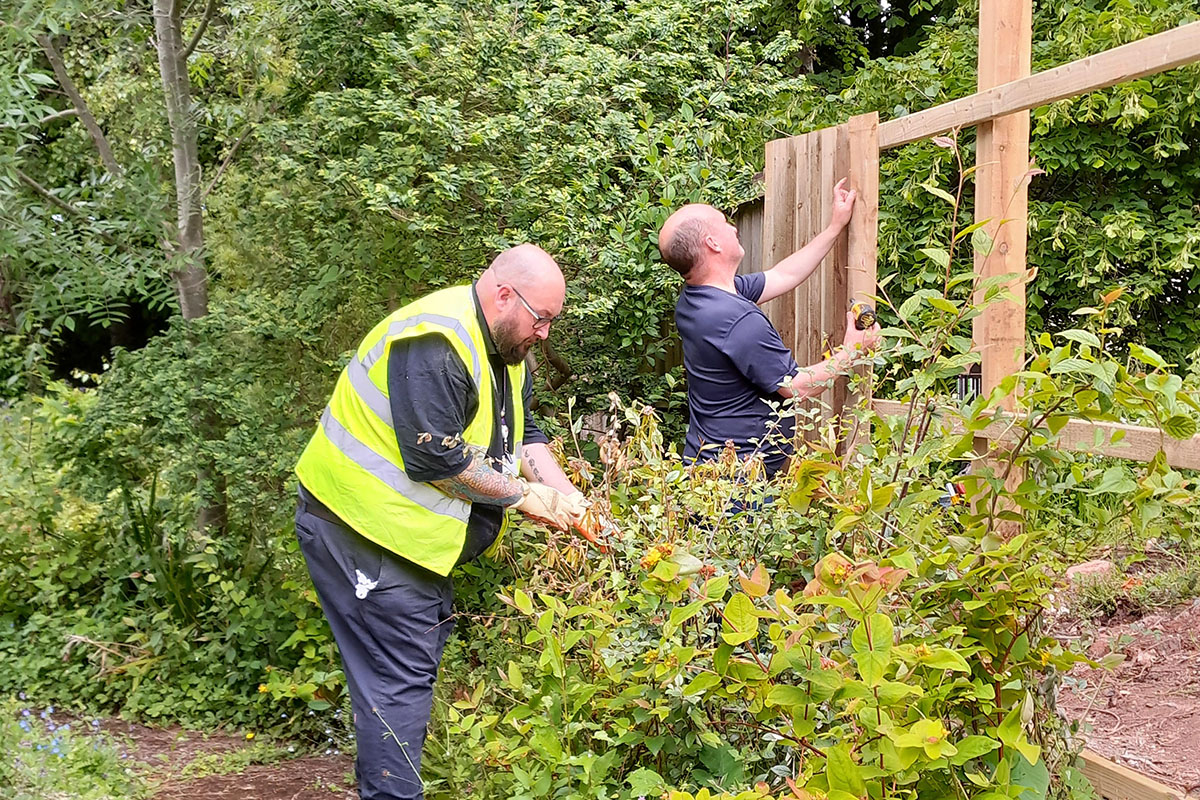 Two Mitie colleagues building a wooden fence and cutting back bushes