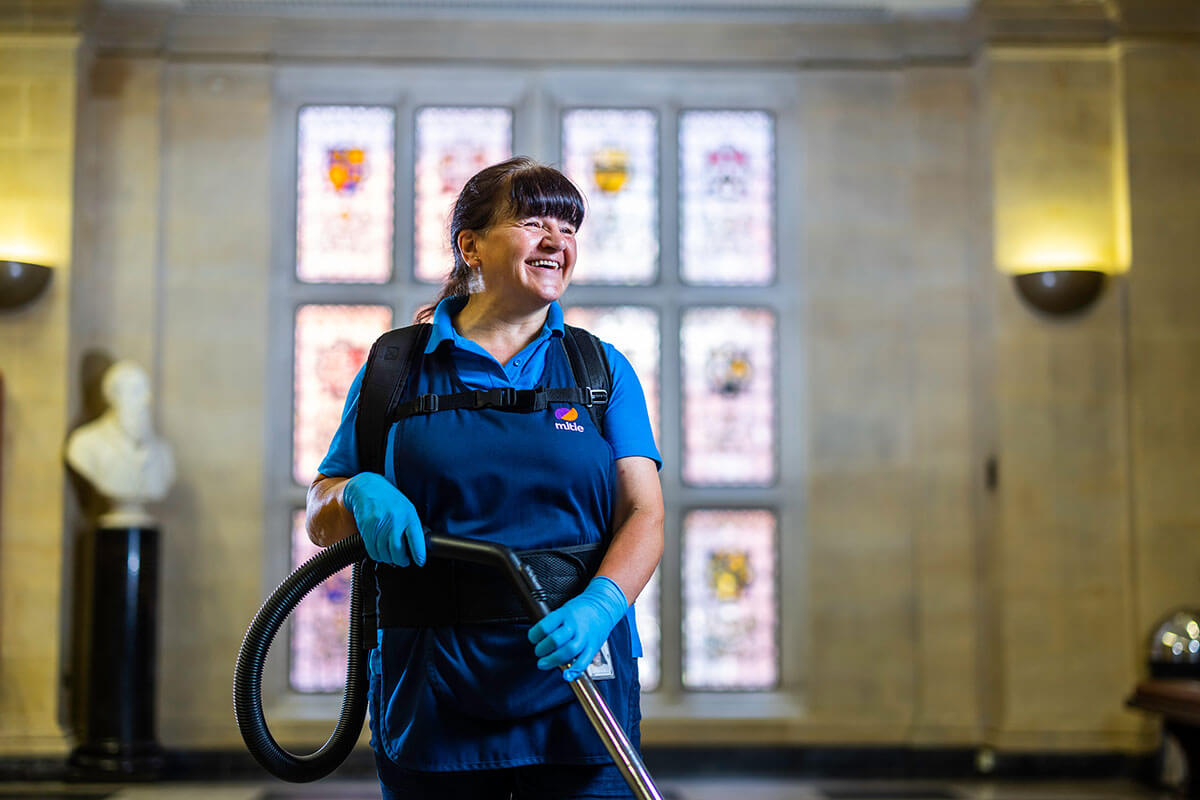 A Mitie female cleaning employee holding a vacuum cleaner in front of stained glass windows