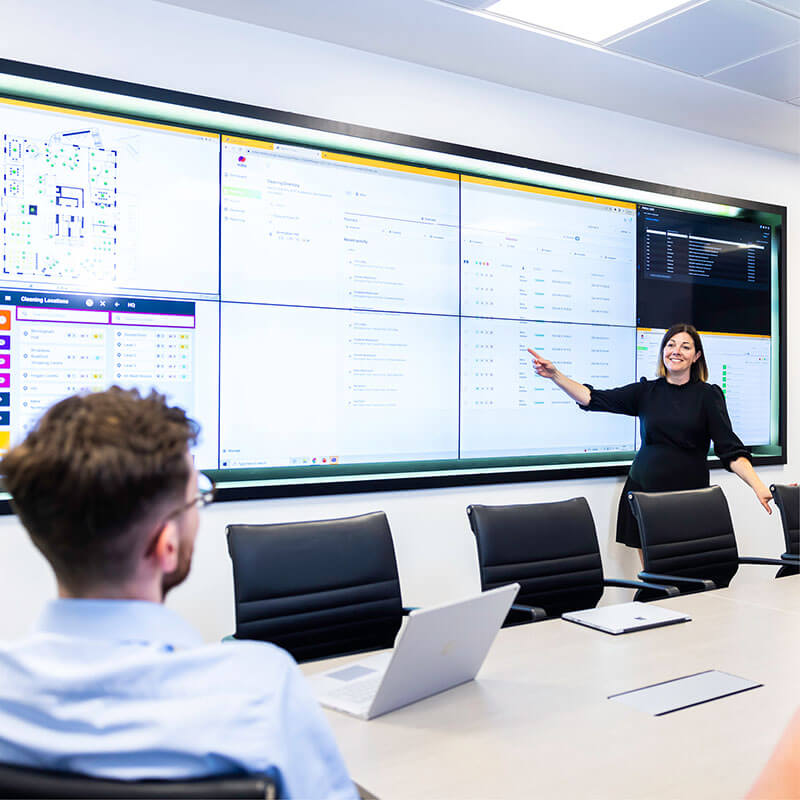 A woman pointing at various charts on a screen in boardroom