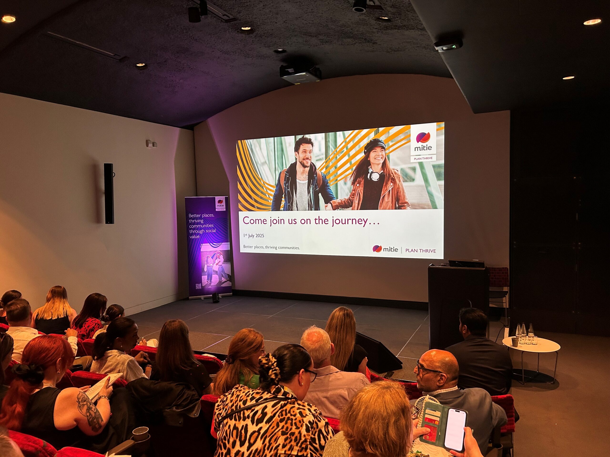 Crowd watching video on TV screen at  Plan Thrive launch