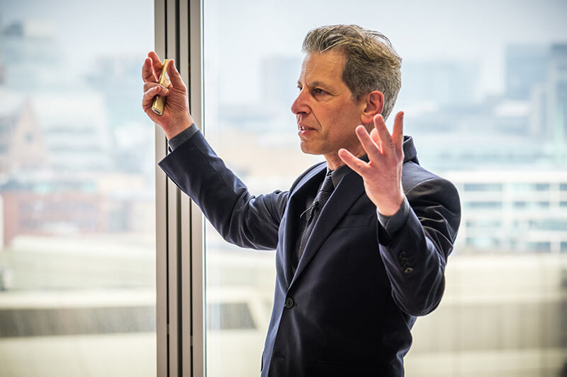 David Rowan, in a dark suit and shirt, gesturing in front of a window in the Shard at a Mitie Carbon Disclosure event