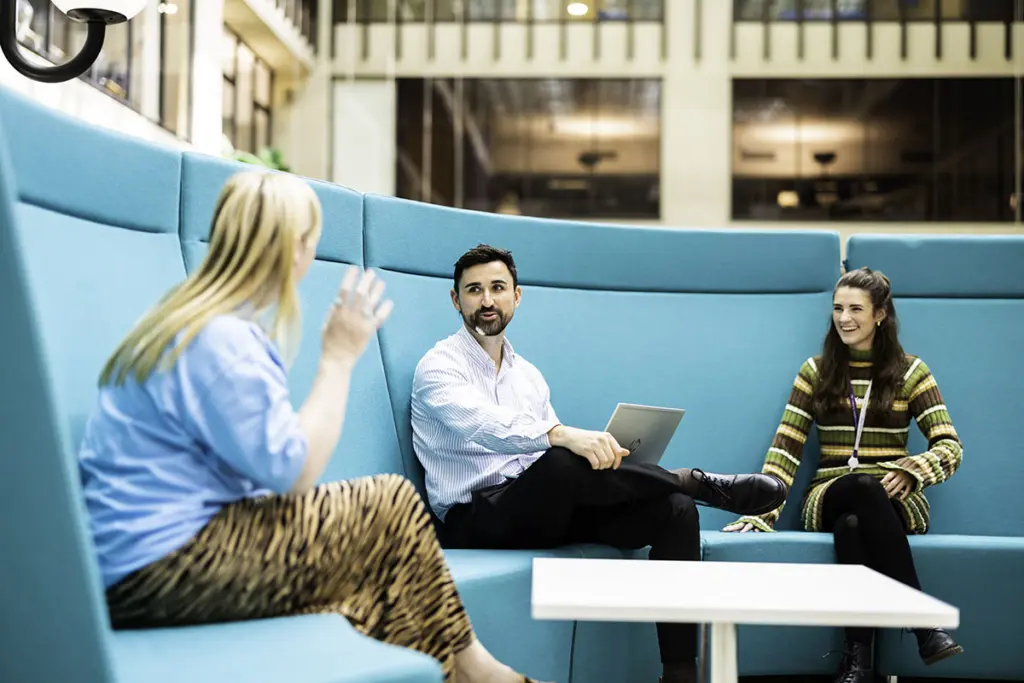 Three people smiling and talking on a sofa