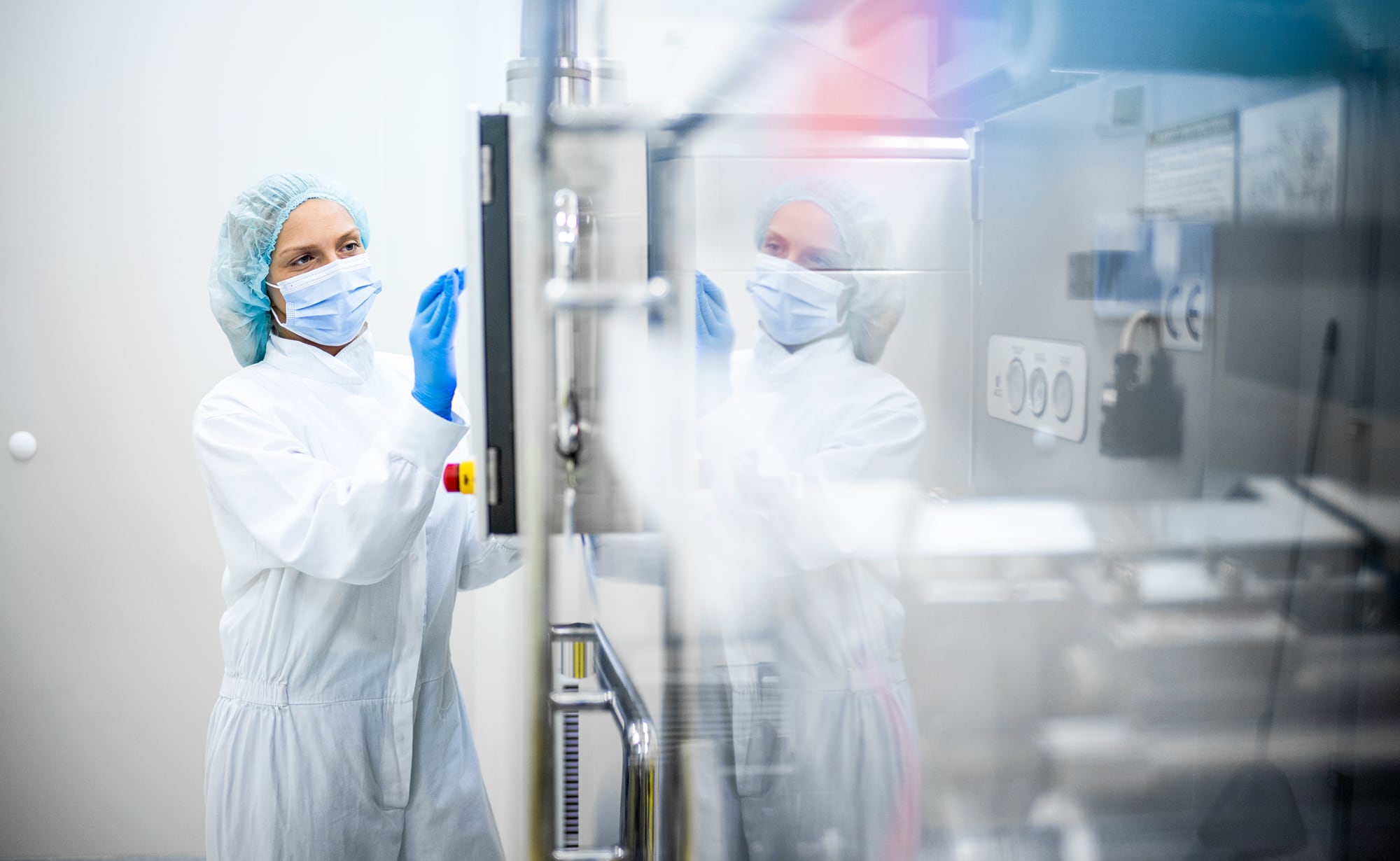 Technician in protective clothing and a face mask operating equipment in a controlled environment.