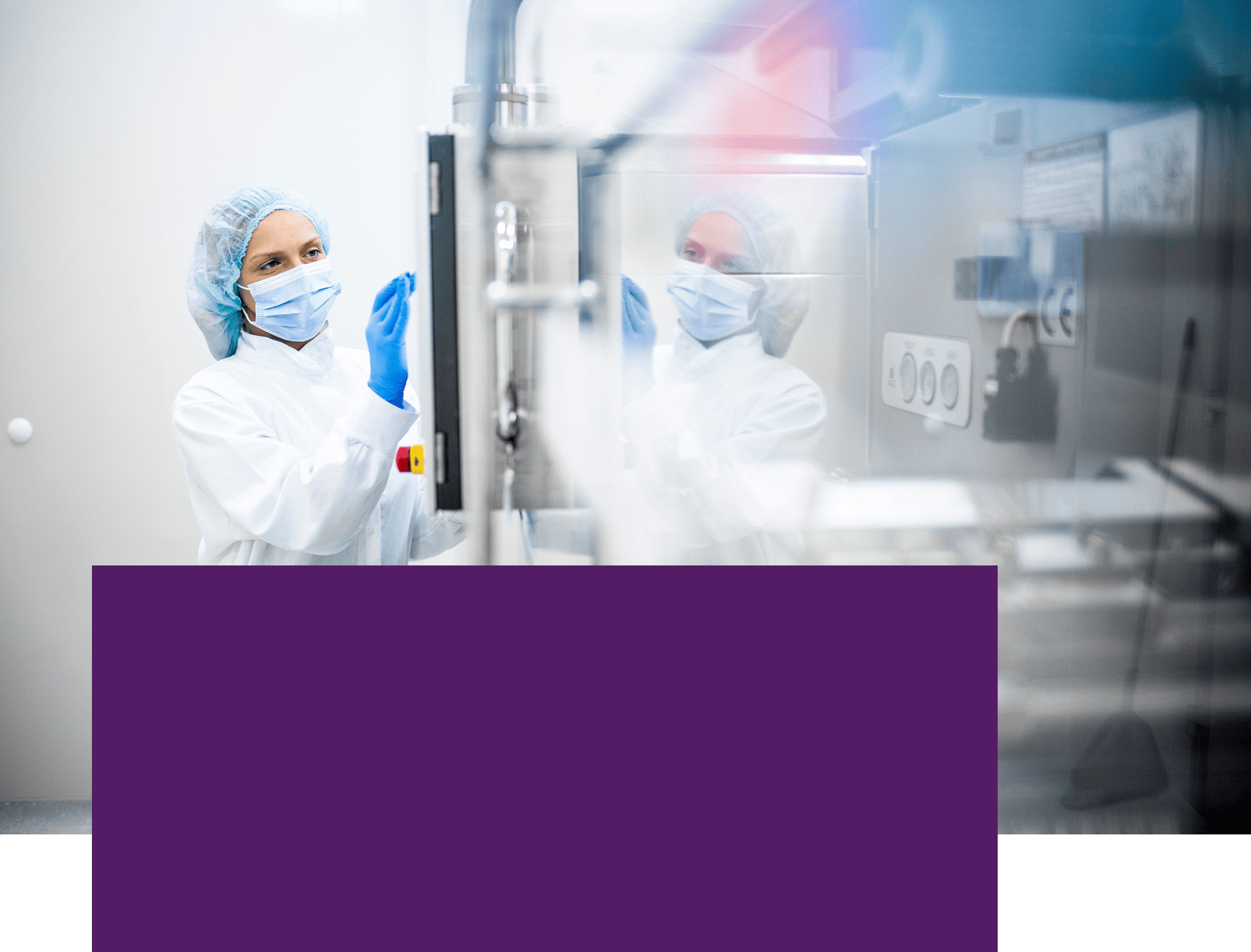 Technician in protective clothing and a face mask operating equipment in a controlled environment.