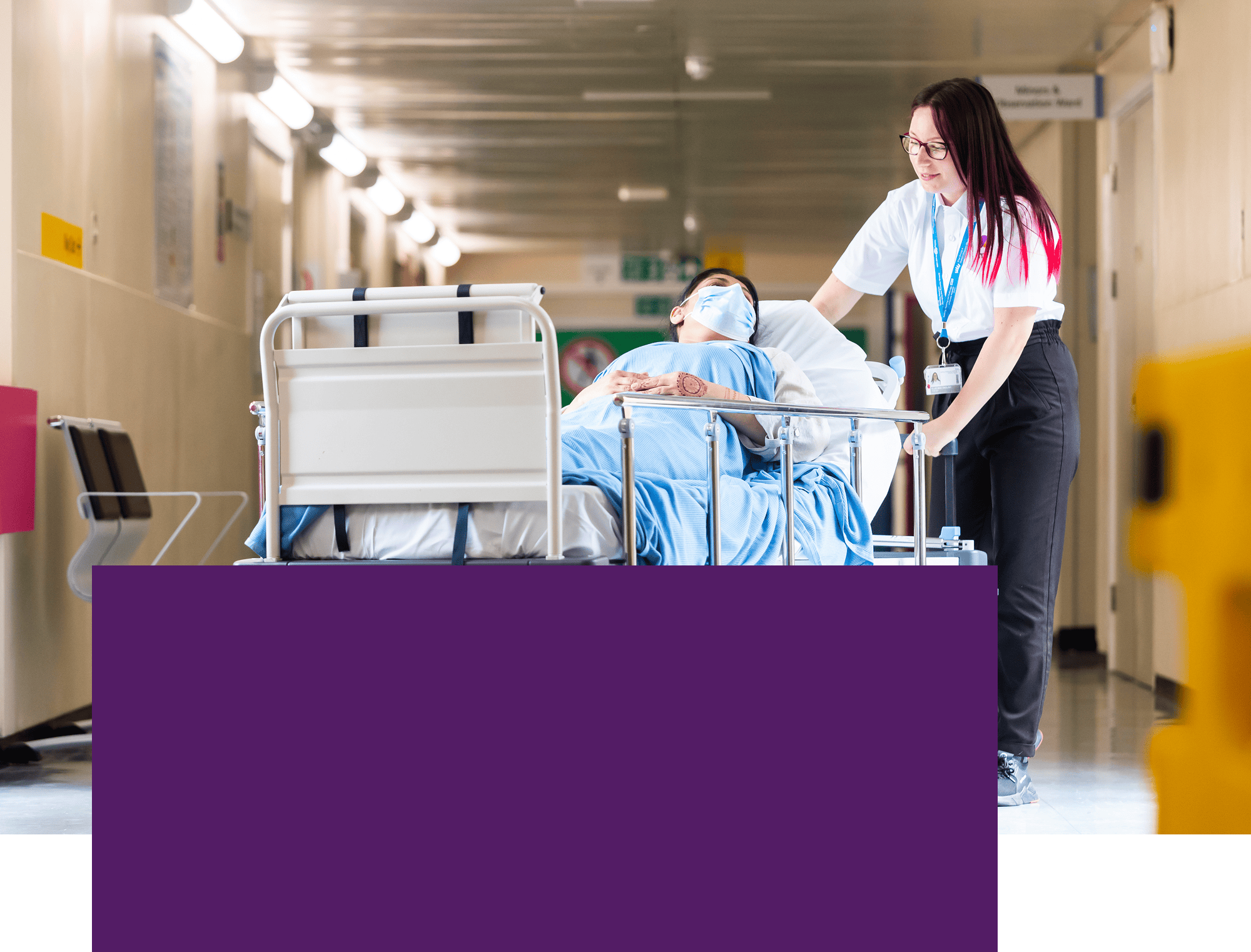 Healthcare worker pushing a patient on a hospital bed along a corridor.