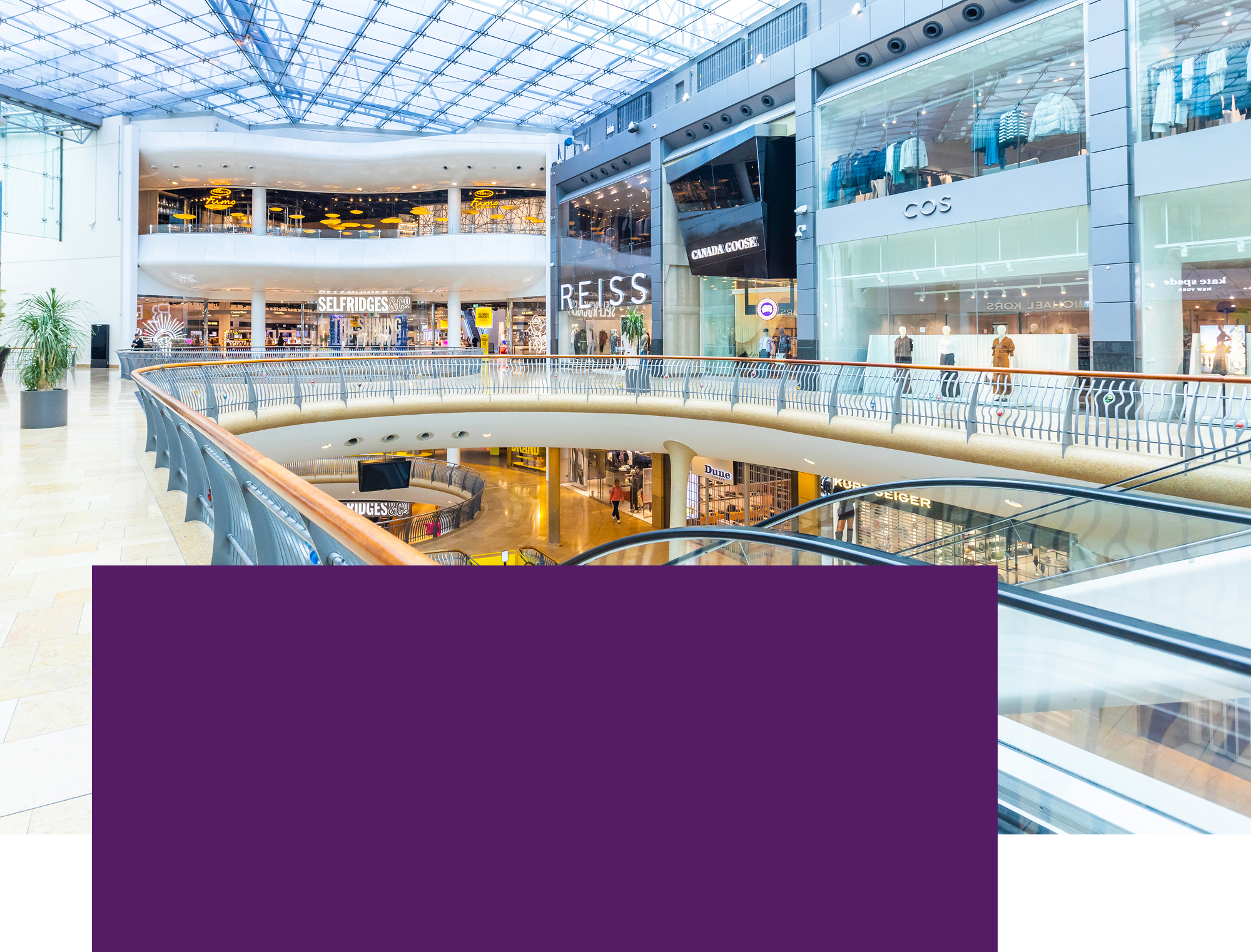 Interior of a modern shopping centre with shops, escalators and multiple levels.