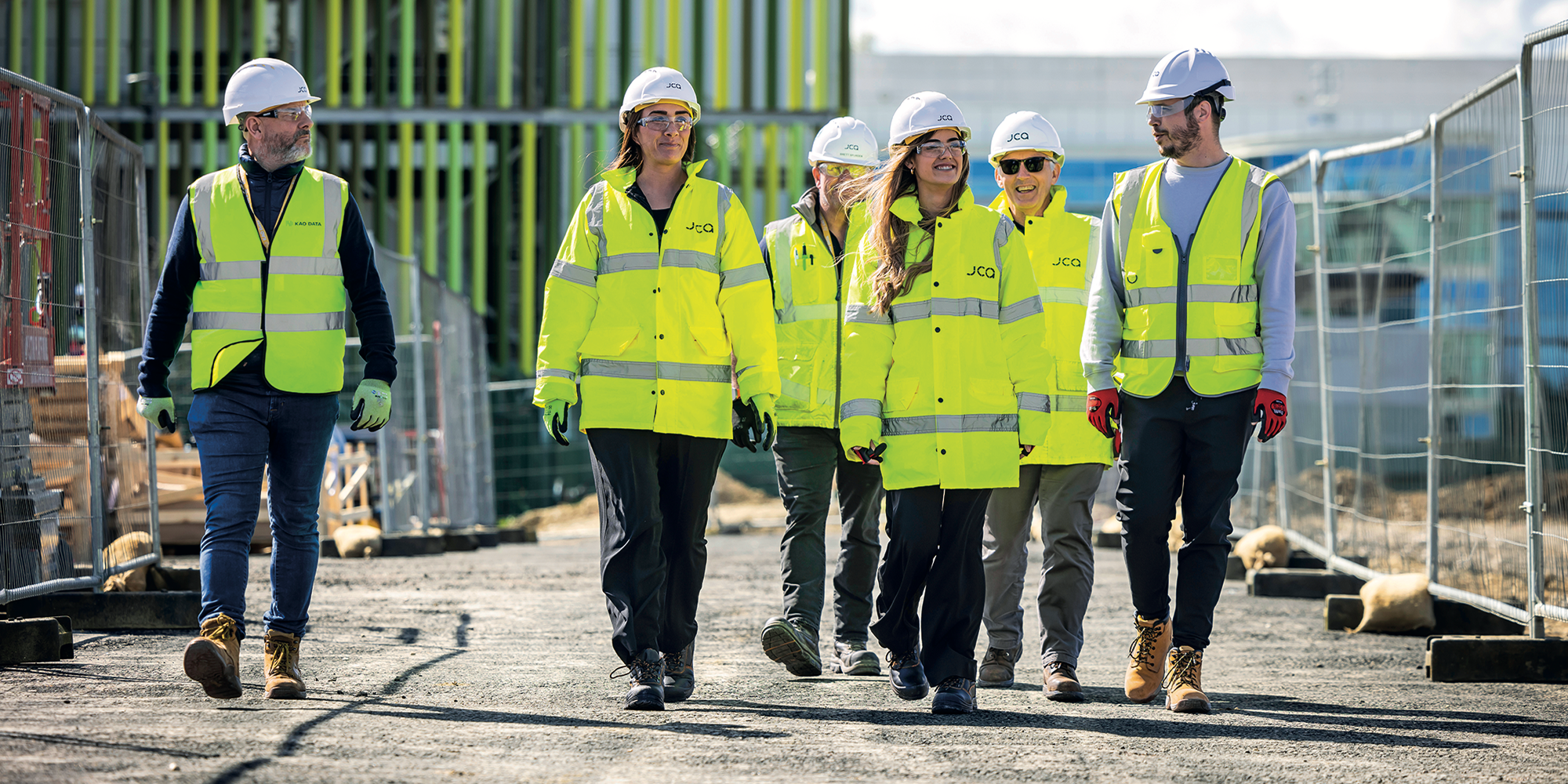 Group of workers in high-visibility clothing and hard hats walking through a construction site.