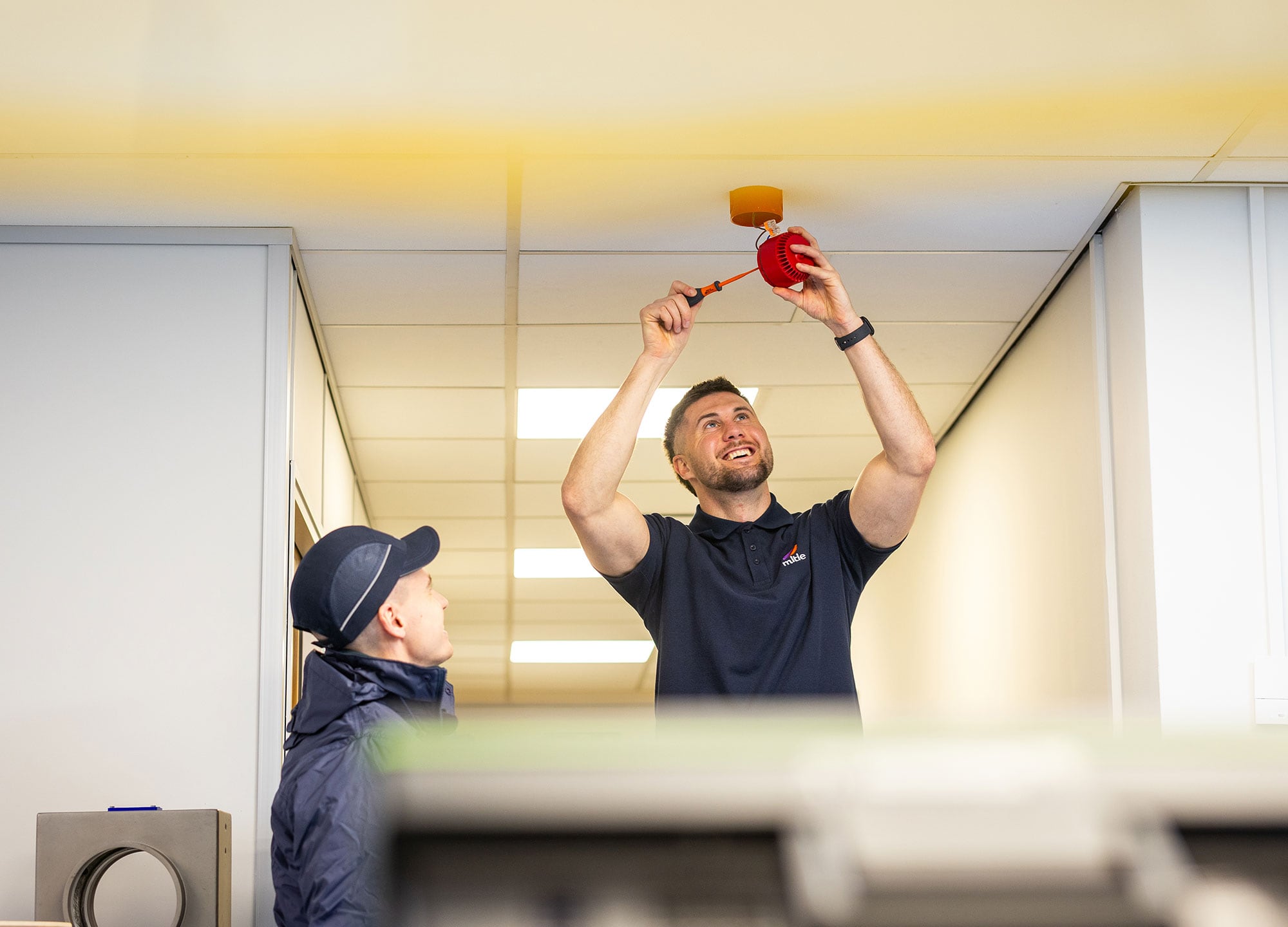 Mitie worker installing fire safety equipment.