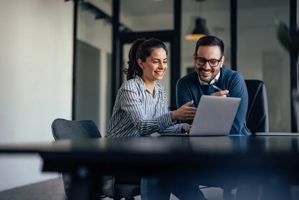 Two people holding a meeting in an office, with a laptop on a desk